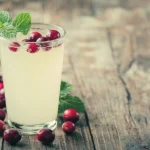 A glass of white cranberry juice on a wooden table with cranberries and mint leaves